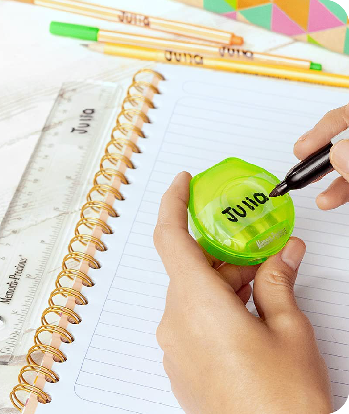 Mano con estuche verde de plástico escribiendo un nombre con plumón sobre una tira de cinta mágica.